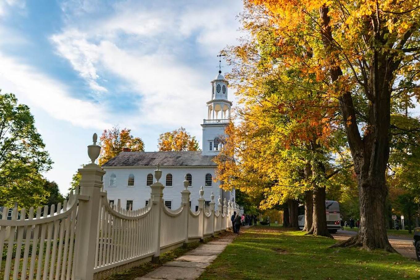 Una iglesia blanca y una cerca de estacas enmarcada por hojas de otoño.