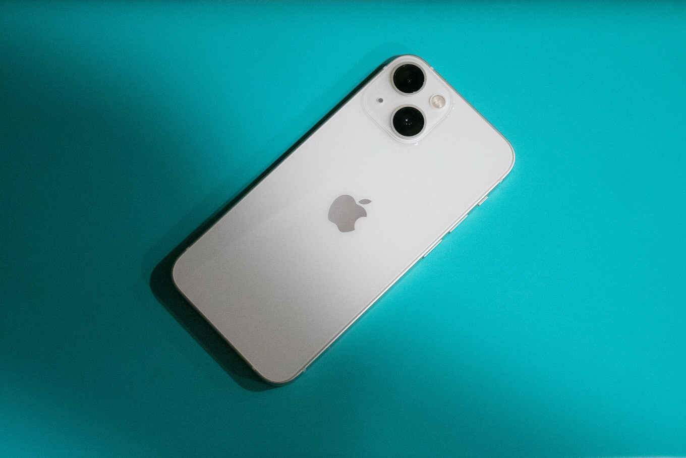 iPhone 13 Mini blanco sobre una superficie verde azulado